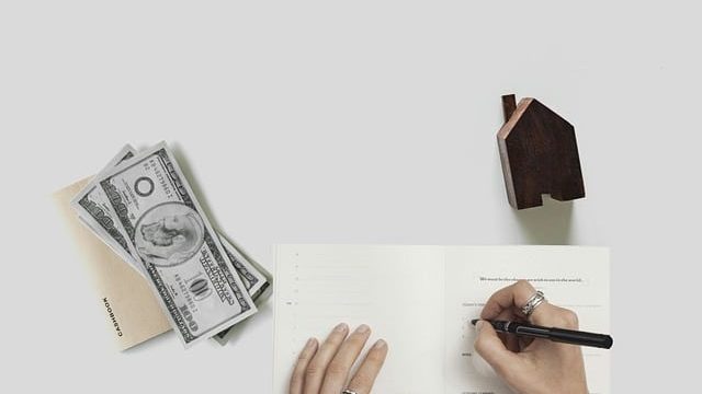 dinero, una casa y una persona escribiendo